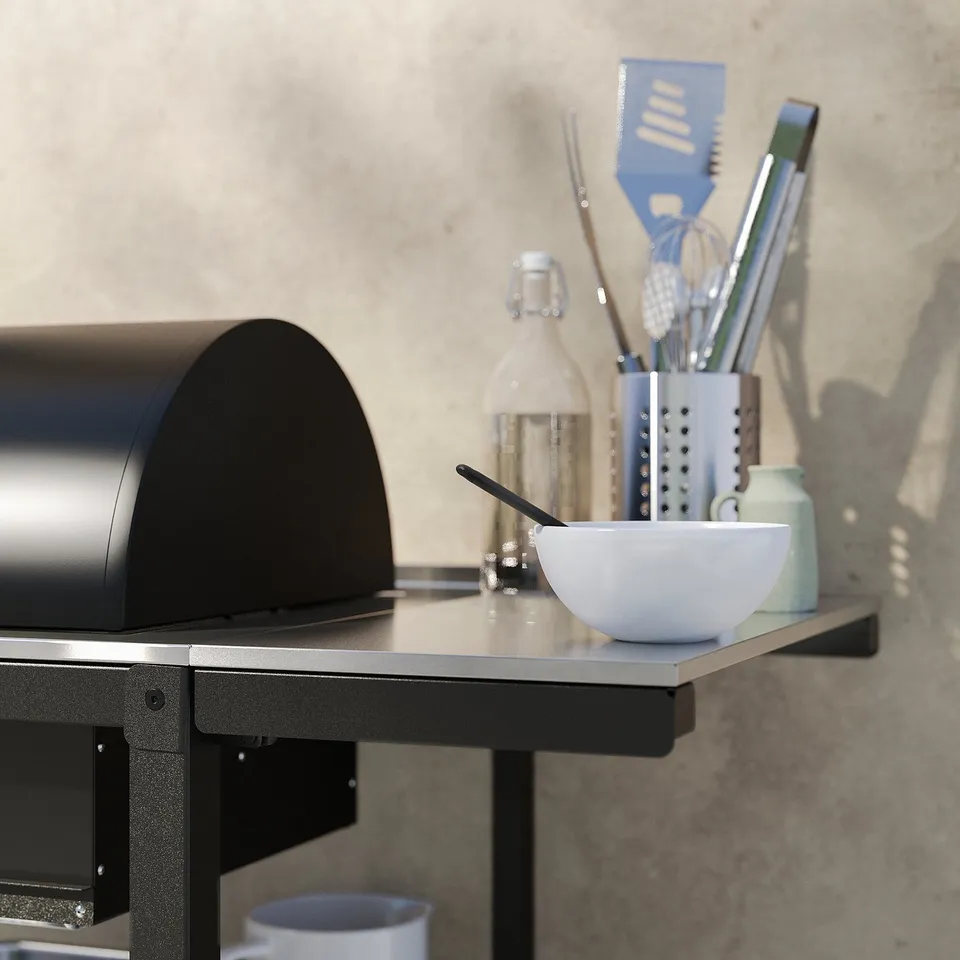 Modern outdoor kitchen with black GRILLSKÄR charcoal grill. White bowl, utensils, and stainless steel sides.