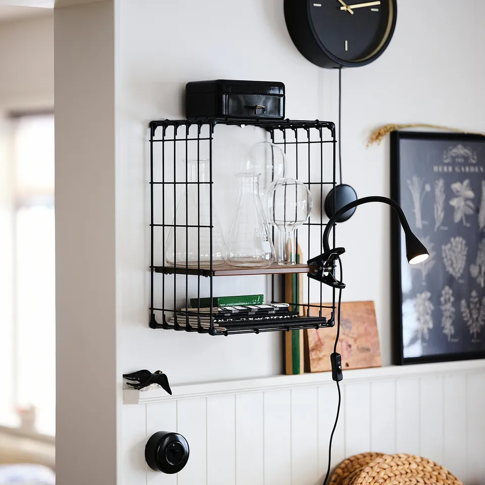 Black clock above shelves with vintage radio, glassware, and lamp.