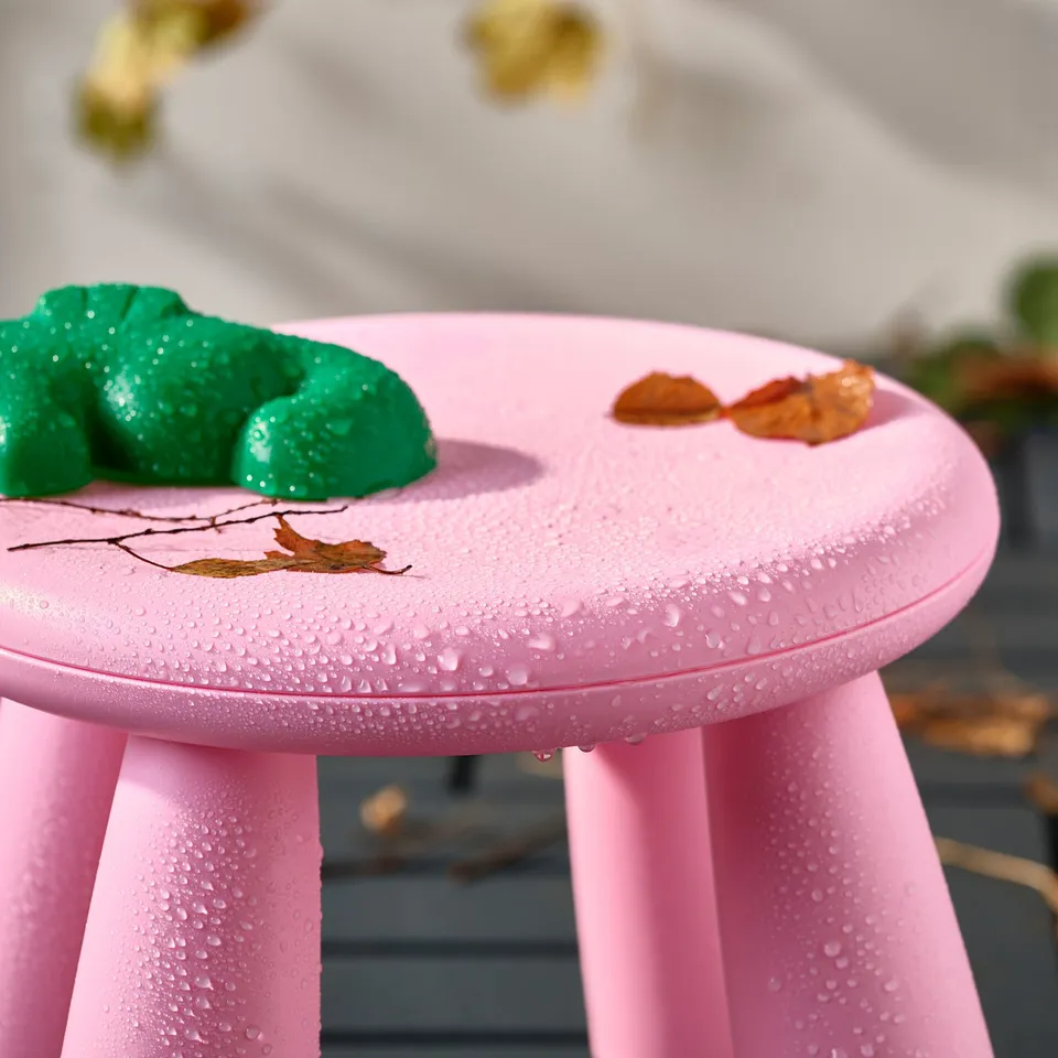 Bright pink kids stool, outdoor use, easy to clean, with green toy and leaves on top.