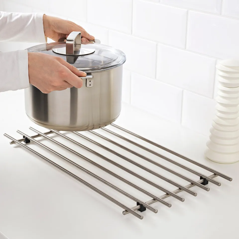 Hands holding a pan with LÄMPLIG trivet, preventing heat and scratches.