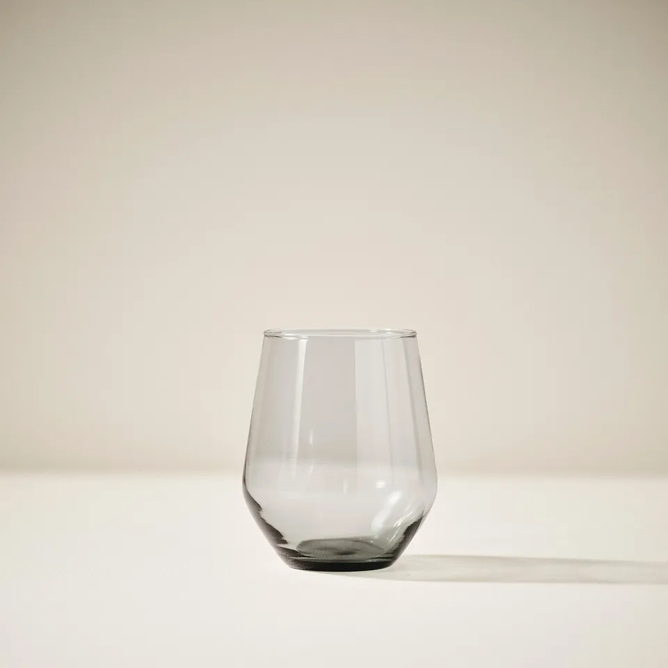 Single, clear glass cup sits alone in soft light, casting a subtle shadow.