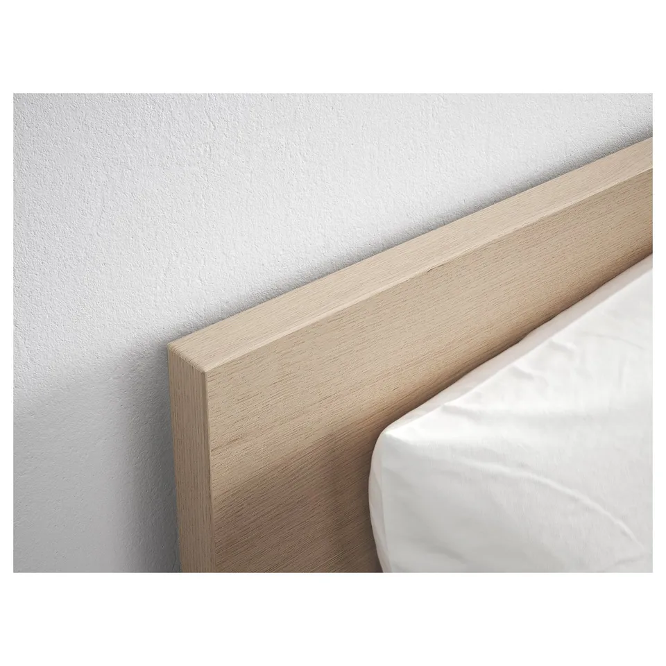 Close-up of a light wooden headboard against a white wall with a white pillow. Shows quality finish and design.