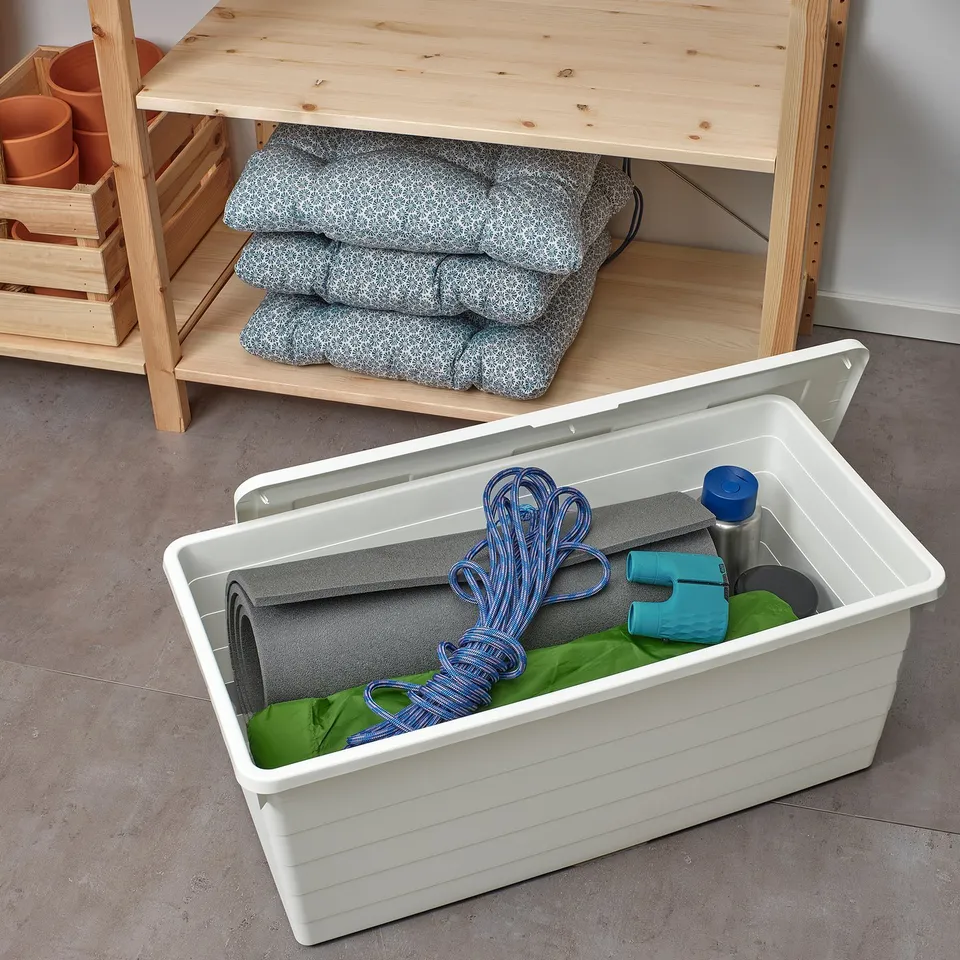 White SOCKERBIT storage box holds camping gear, beneath wood desk with blue bedrolls.