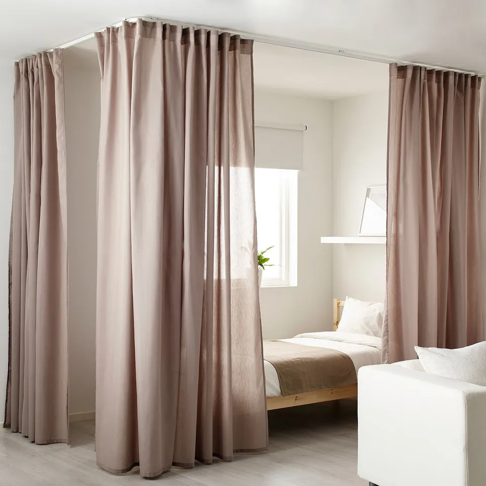 Minimalist bedroom with VIDGA curtain rail, wooden bed, white linens, and greenery.