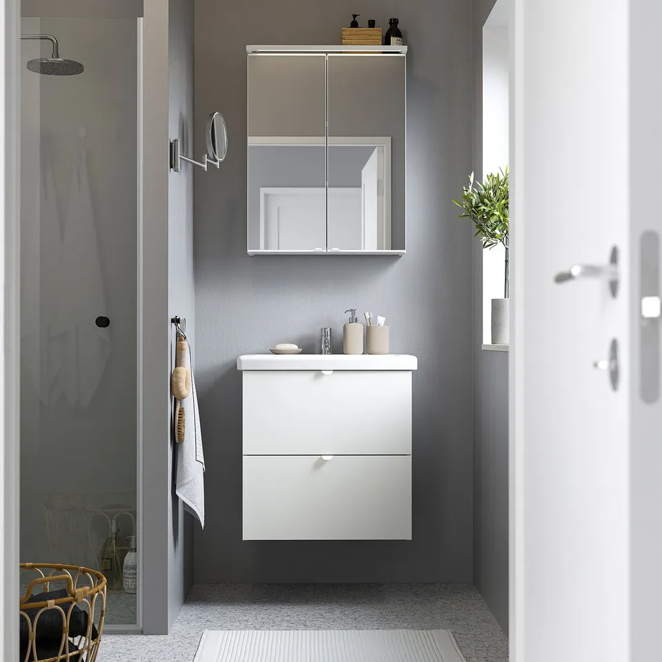 Modern bathroom with white ENHET wall-mounted cabinet. Sits below mirror, larger than towels hung nearby.