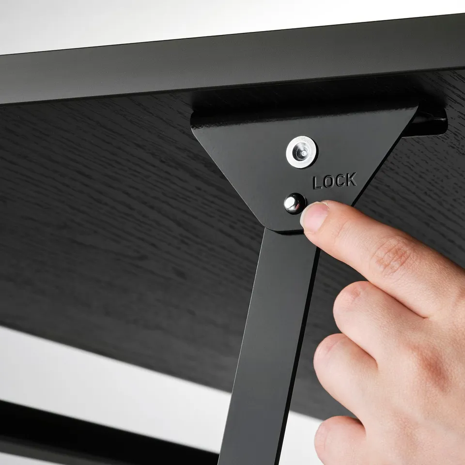 Image depicts a persons hand adjusting a locking mechanism on a black adjustable coffee table, showcasing its functional height adjustment feature.