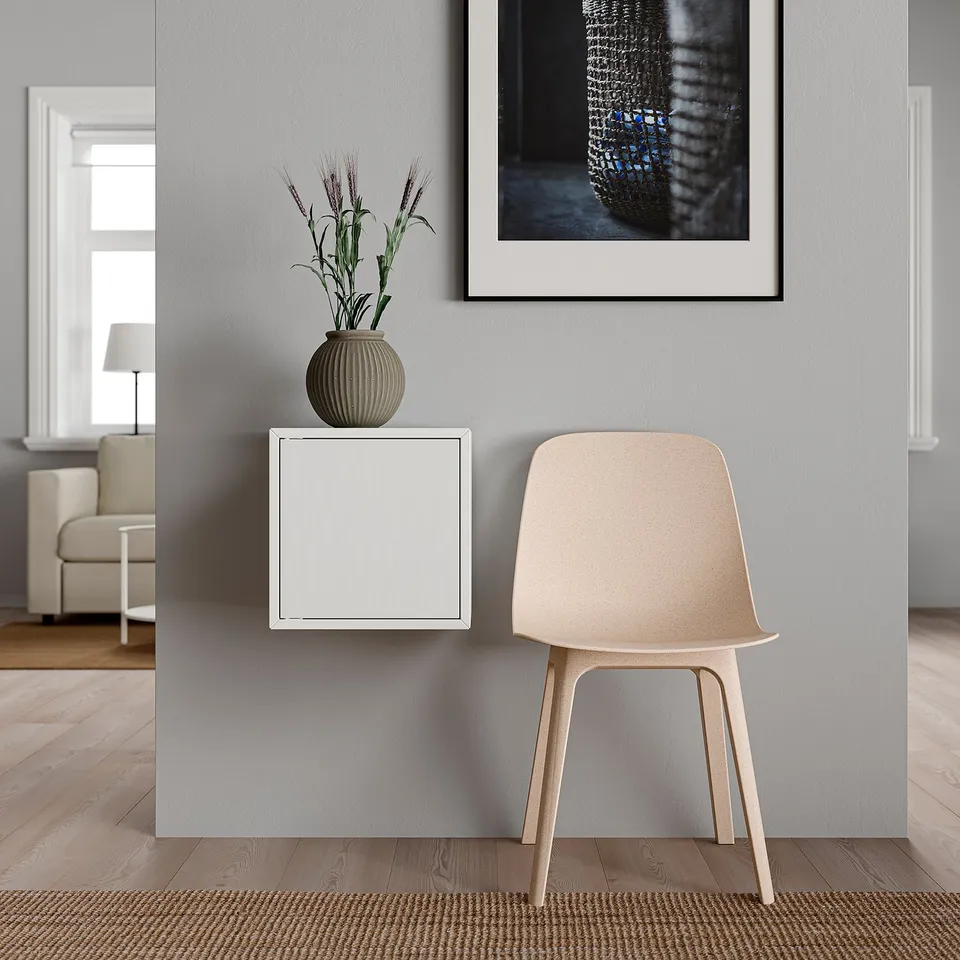 Minimalist room with white EKET cube shelf, beige textured chair, grey wall, and framed art. A small potted plant sits atop the shelf.