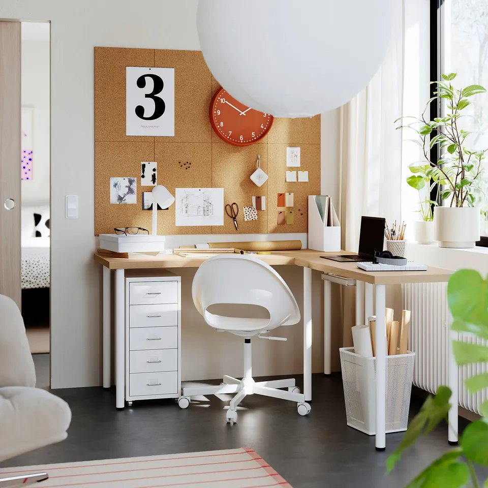 Home office with light desk, plants, small white chair, clock, organised storage.