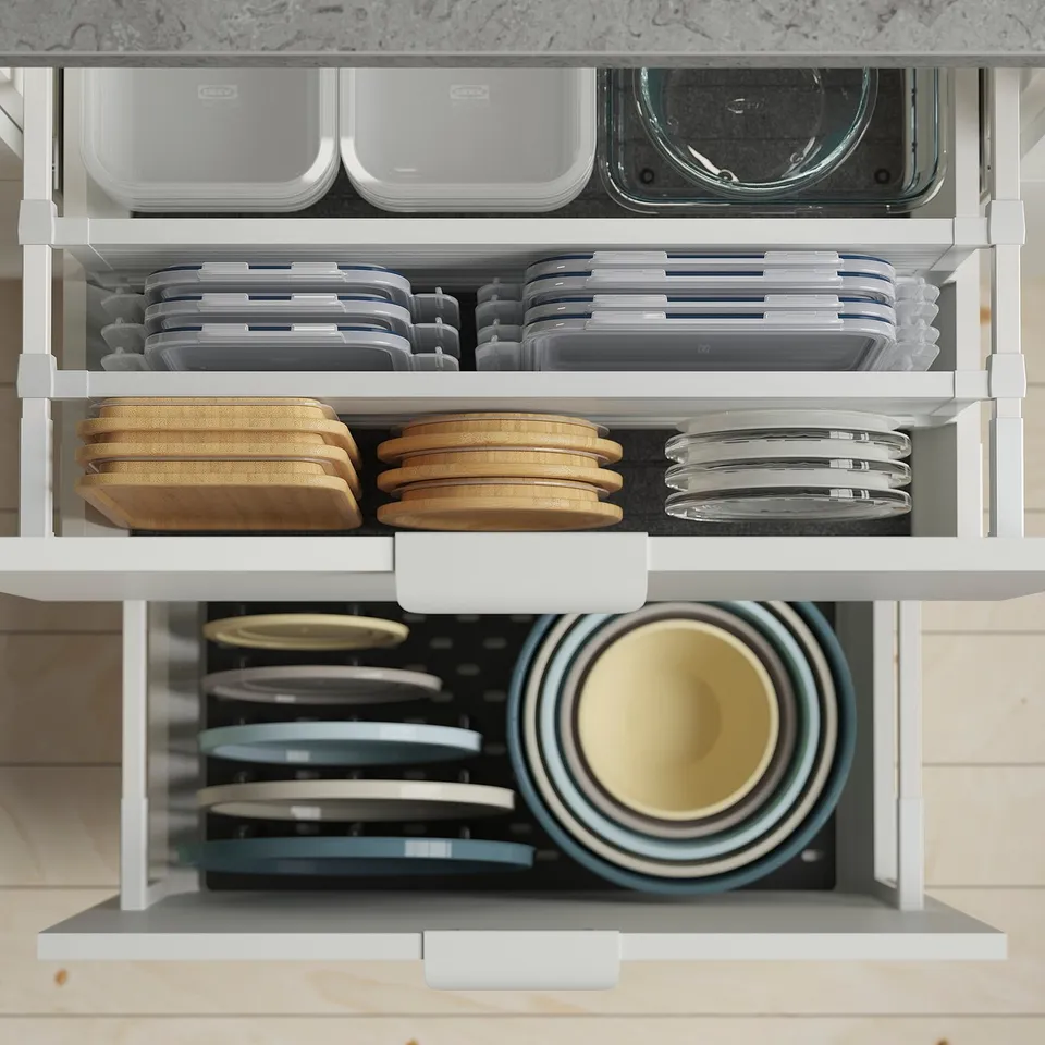 Organised kitchen cabinet with stackable containers and lids for dry food storage. Bowls of varying sizes are neatly arranged on white shelves.