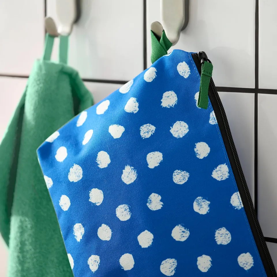 A blue toiletry bag with white dots hangs on a hook. The zip is green, and the bag has multiple compartments.