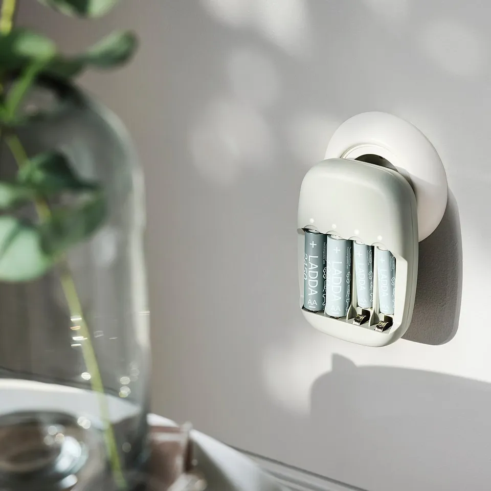 A white STENKOL battery charger hangs on a wall, ready for use. A green plant in a clear vase is nearby.