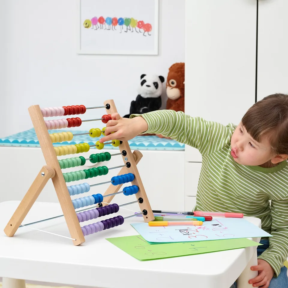 Child plays with colourful abacus on white table.