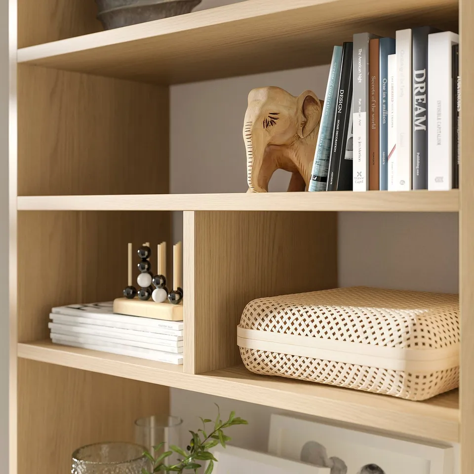 Light wooden bookshelf with various items: carved elephant, books, candles, plant, and wicker basket.
