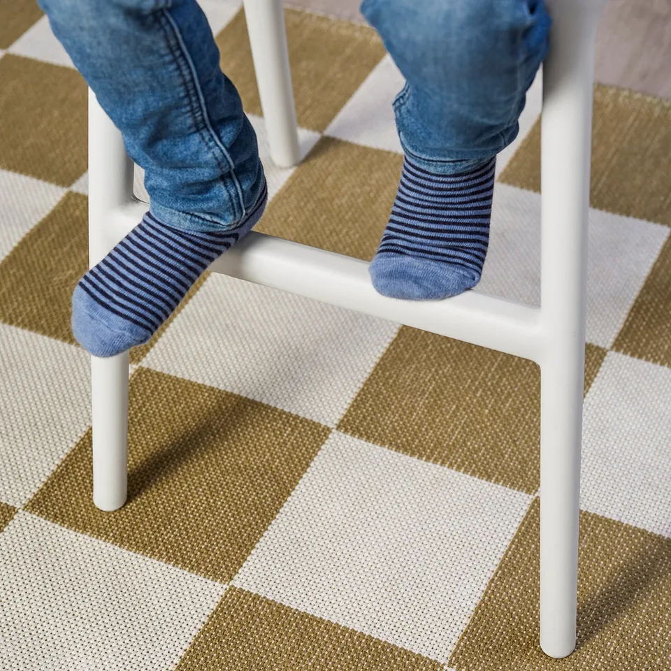 Childs legs dangling from a white junior chair, wearing blue jeans and striped socks. The chair lifts them to dining table height.