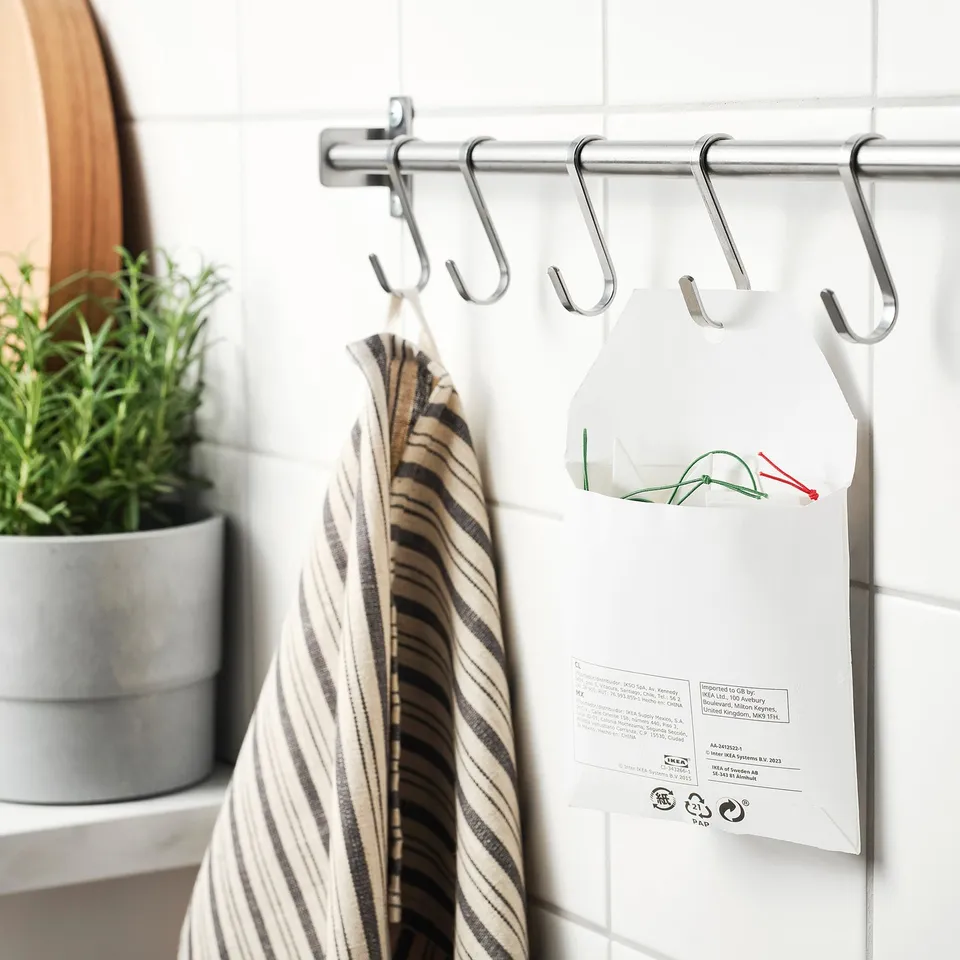 Striped towel and labelled bags hang from chrome s-hooks on a shower curtain bar, showing FÖNSTERFIKUS reusable labels.
