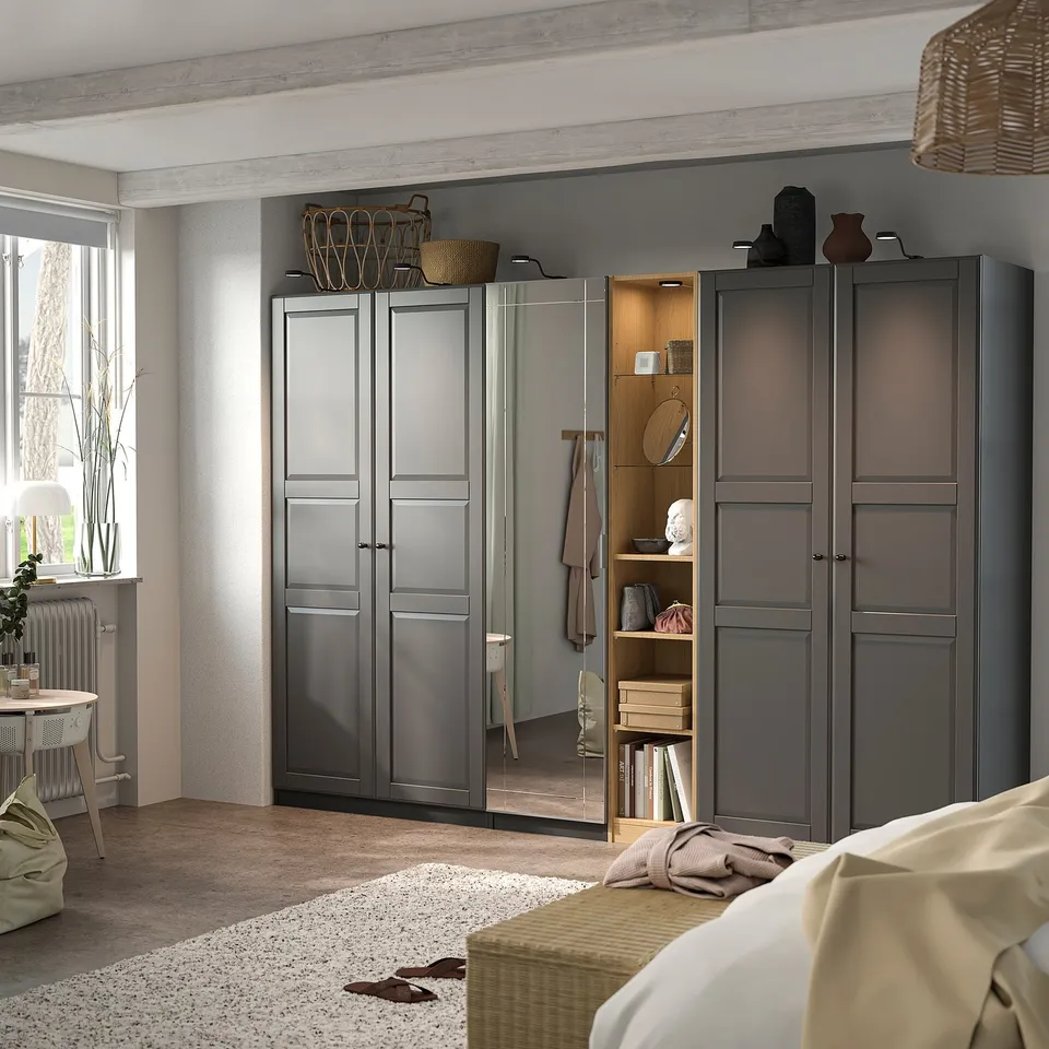Grey PAX wardrobe with mirrored & solid doors, glass & wood shelves, adjustable feet, near bed & window.