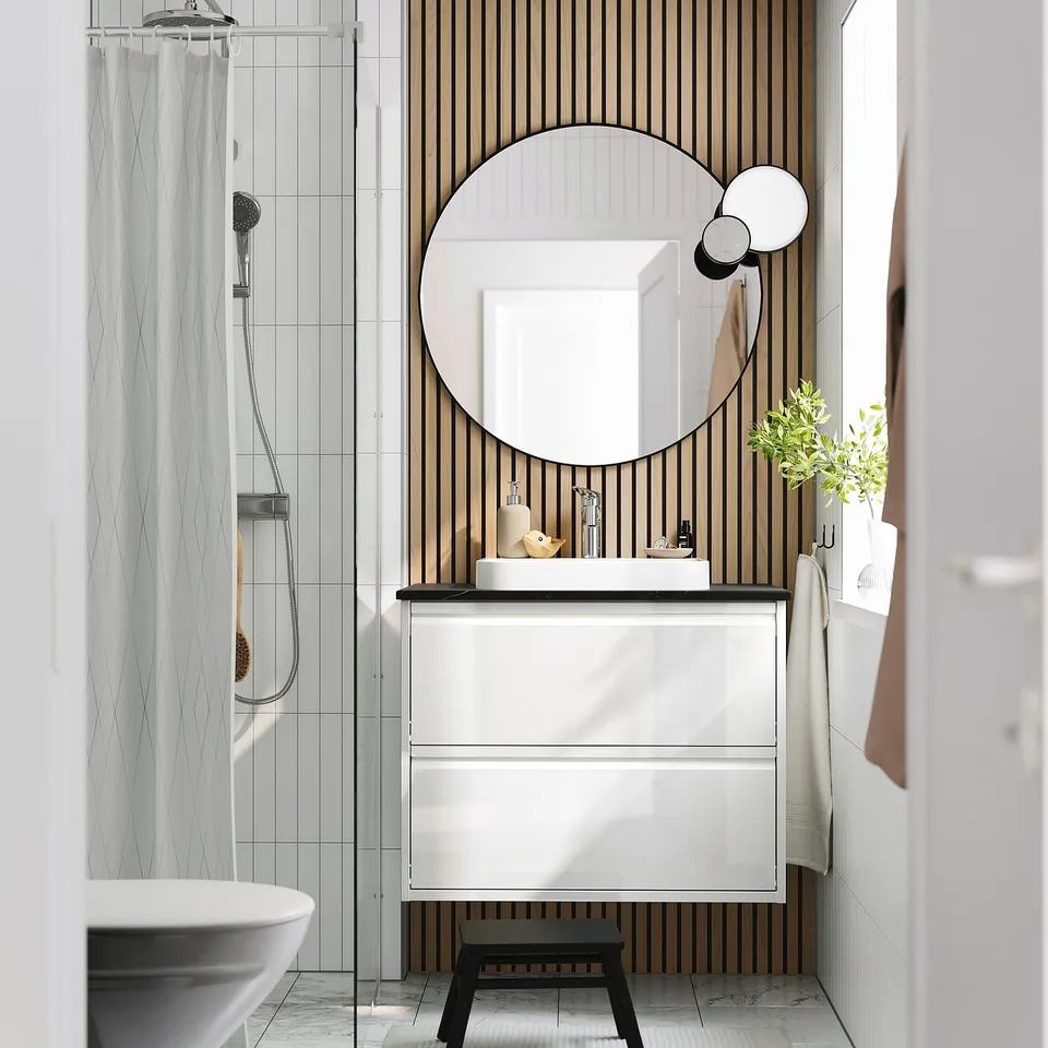Modern minimalist bathroom with white ÄNGSJÖN washstand, marble basin, wooden wall, and round mirror.