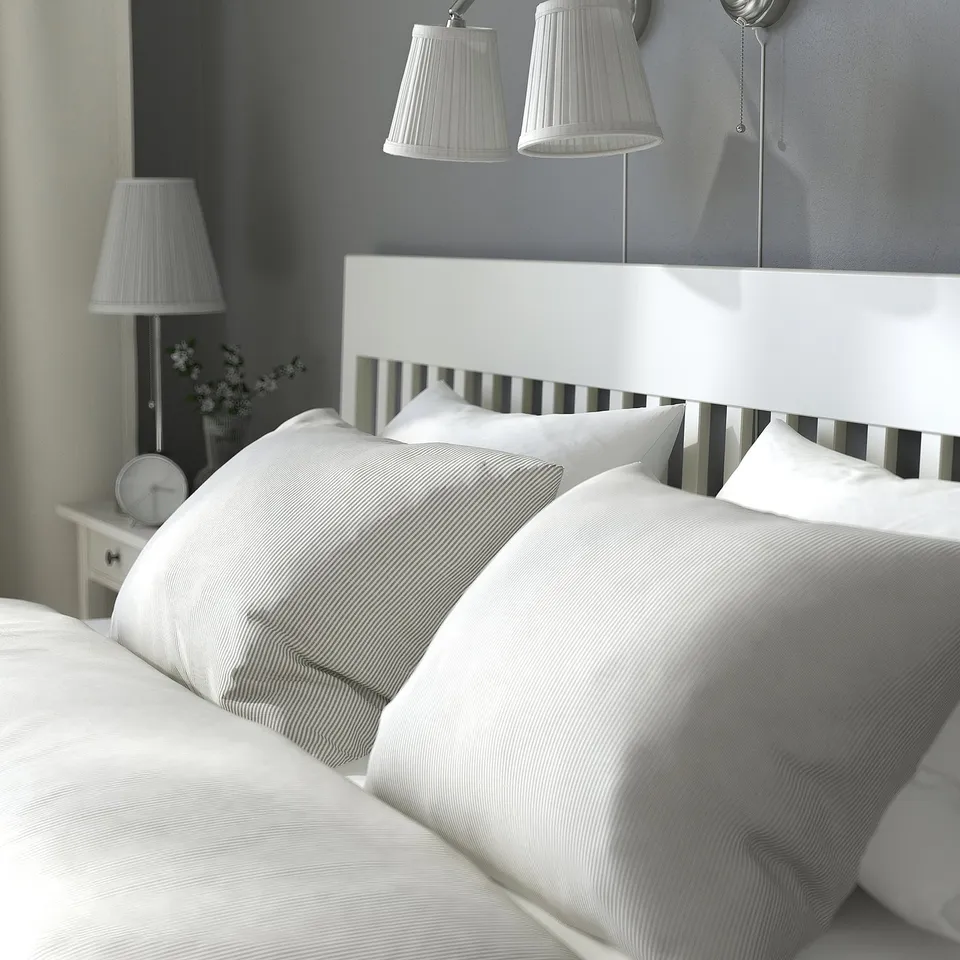 Minimalist white bed with striped pillows; wall-mounted lamps nearby.