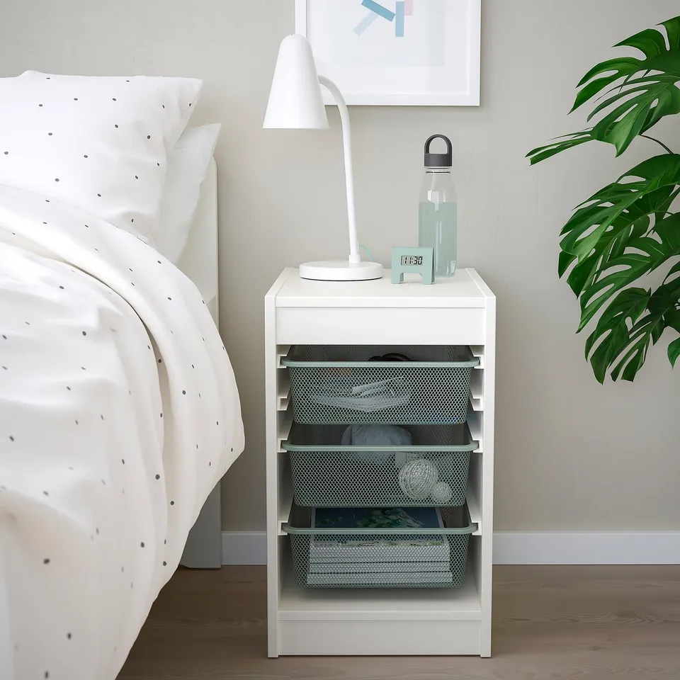 White TROFAST bedside table with lamp, water bottle, plant, mesh storage, next to bed.
