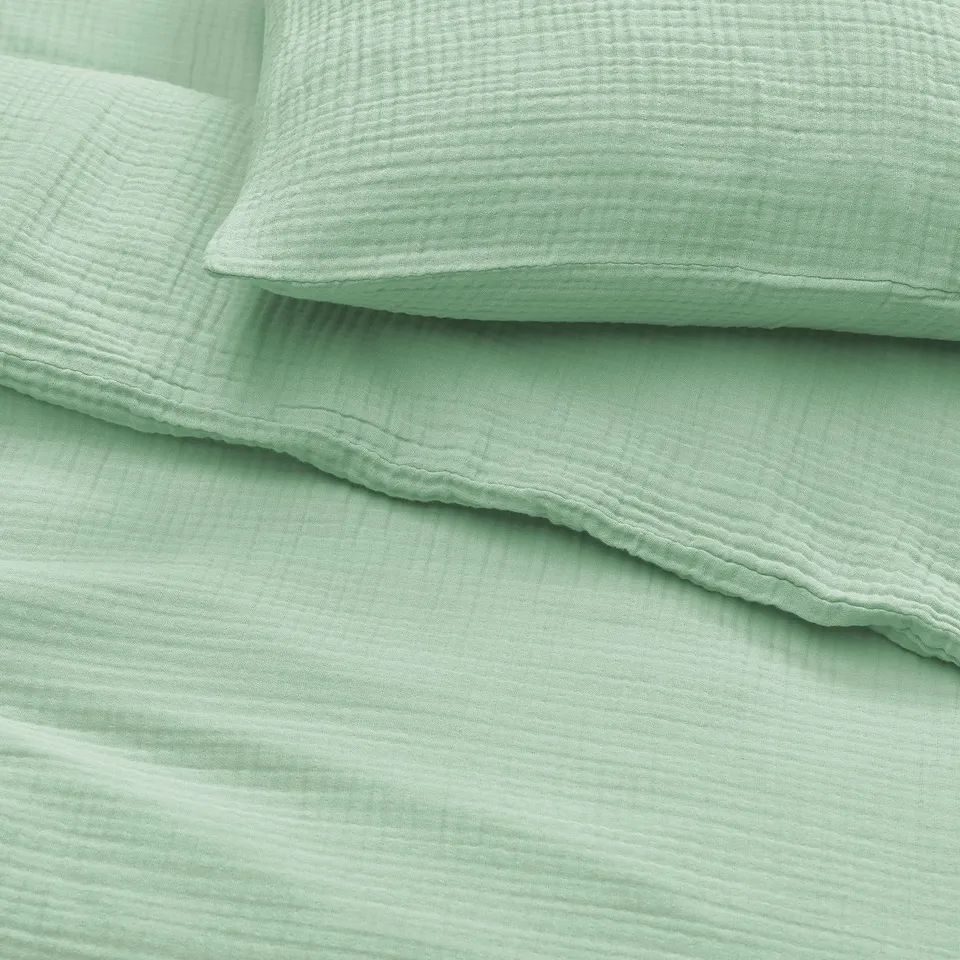 Soft green organic cotton bedding with wavy texture, pillows stacked neatly. Breathable, comfortable design.