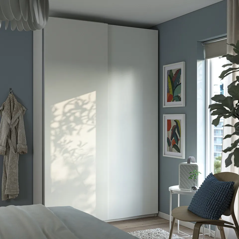 Modern bedroom with large white PAX closet, grey walls, abstract art, cosy chair, blue pillow, plant, and large window.