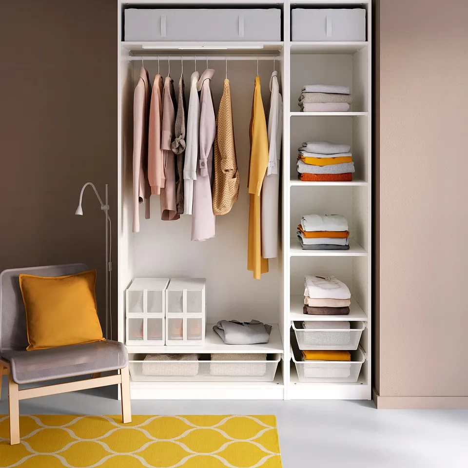 White PAX wardrobe with clothes, grey chair, yellow pillow, yellow rug.