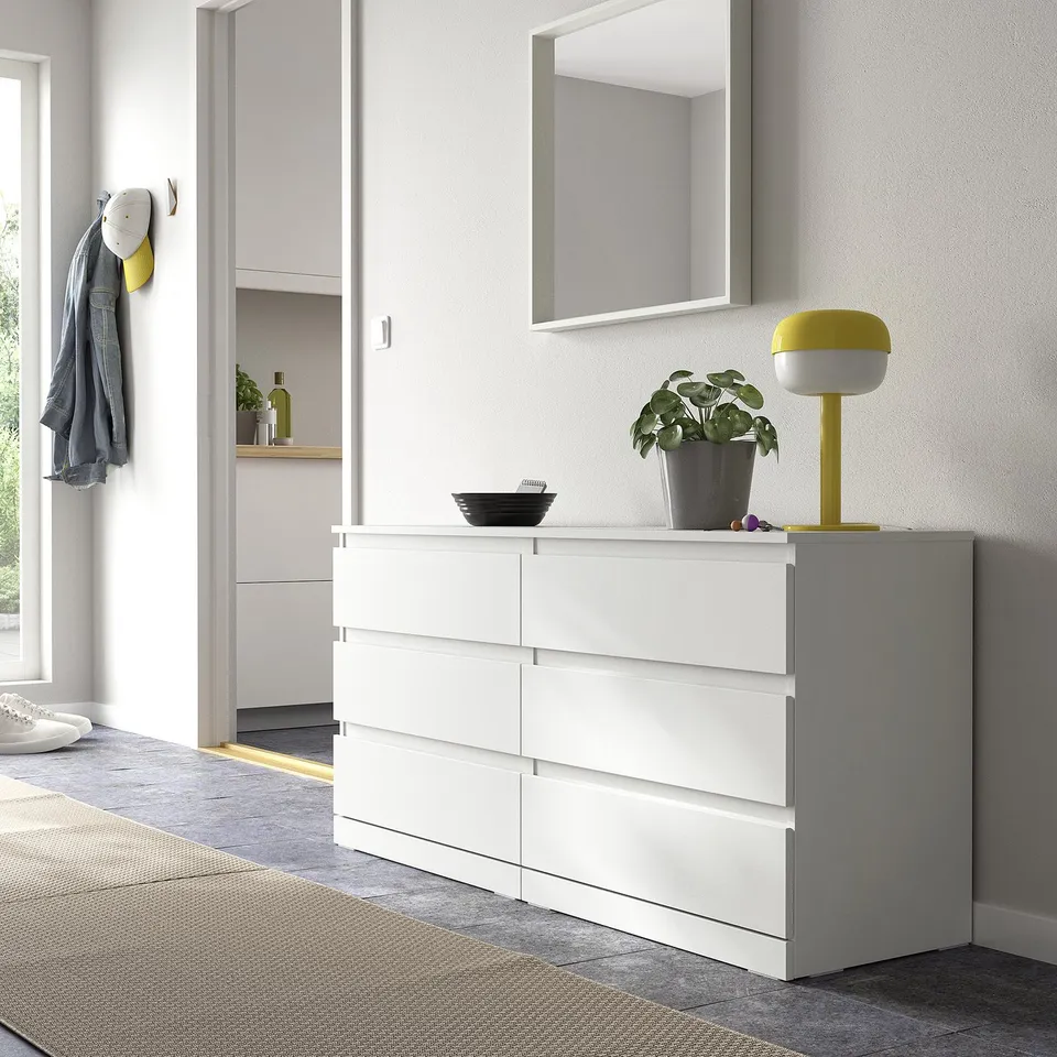 White LILLBERGET 6-drawer chest, simple design, with lamp, plant, jacket nearby.