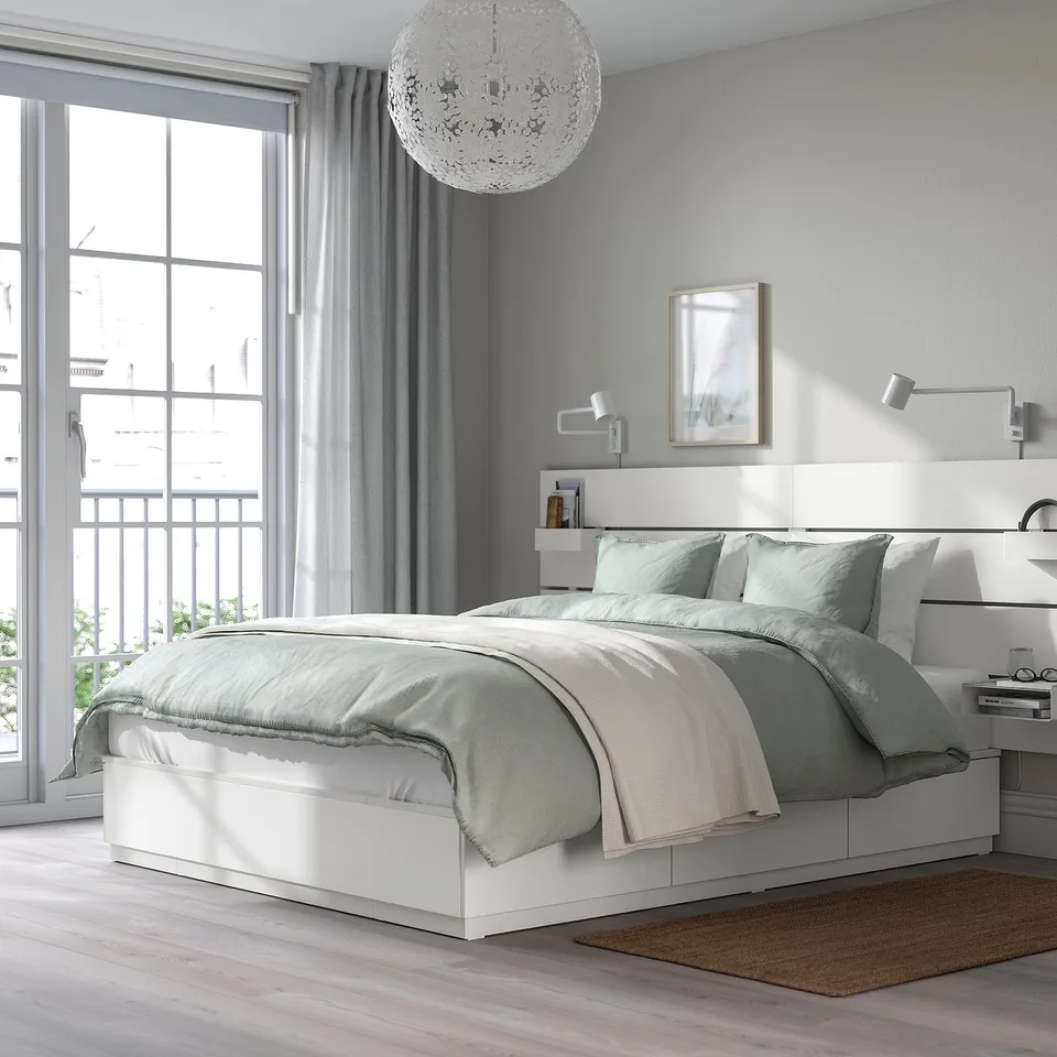 Modern bedroom with NORDLI bed, grey/white linens, chandelier, wall lamps, grey curtains, and balcony view.