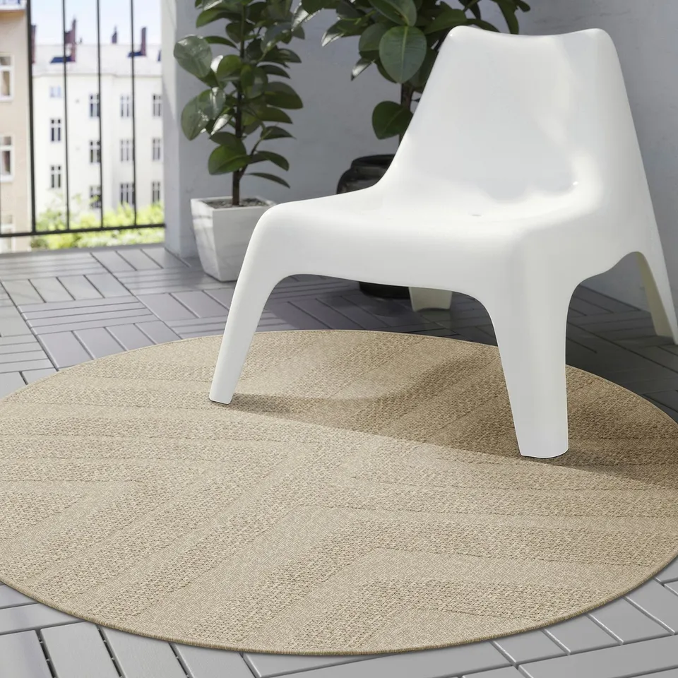 FULLMAKT outdoor rug: white chair on thin, round beige rug. Perfect for balcony or patio. Easy to clean and weather-resistant.
