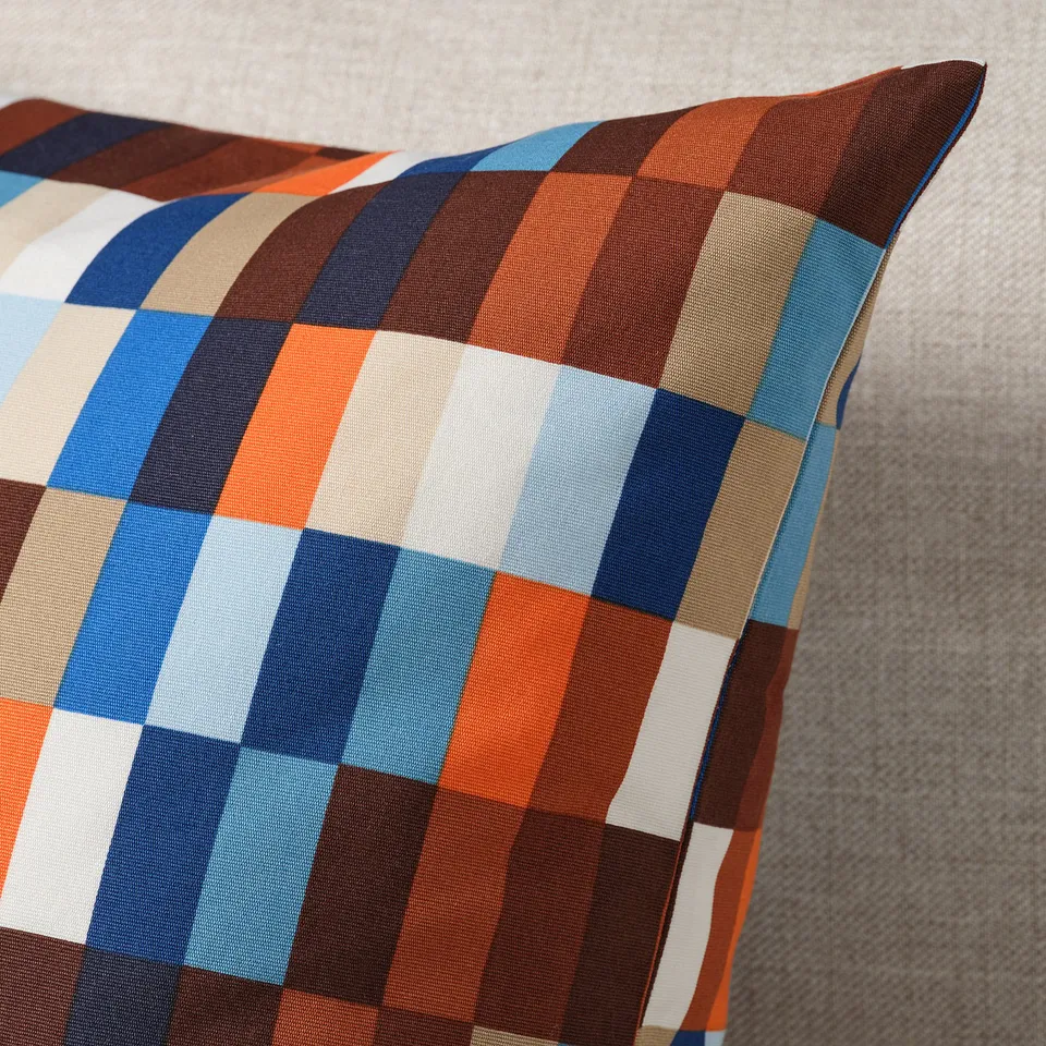 Colourful chequered pillow on a grey fabric; showcase intricate patterns & quality cotton texture.