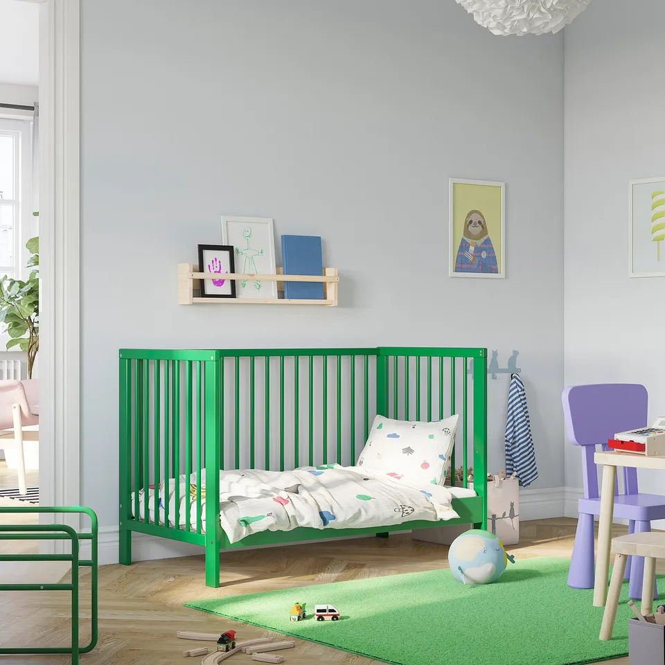 Kids room with green GULLIVER cot. Bright decorations, toys, and fun rug.