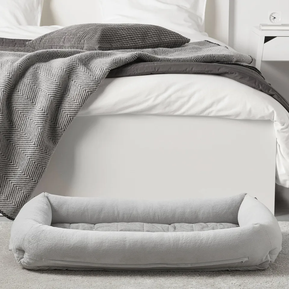A soft dog bed beneath a bed, offering comfort and support. It has a plush interior and raised sides for relaxation.