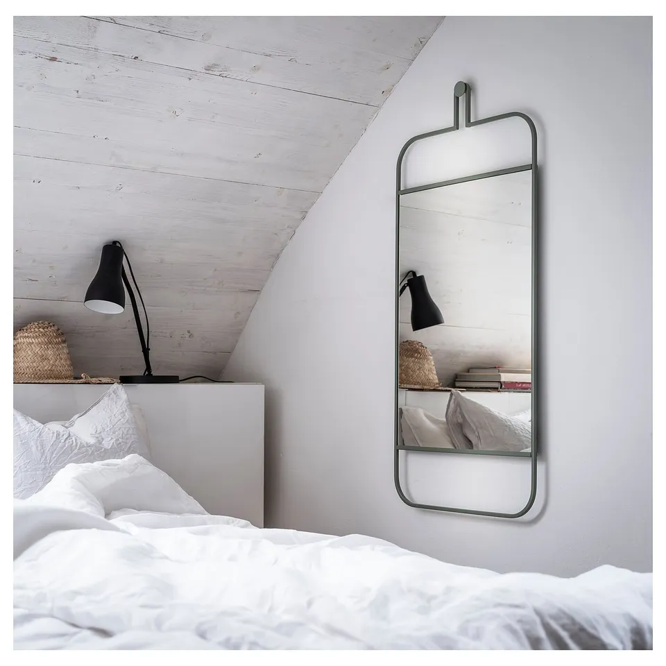 A modern bedroom with a wall-mounted GRANVÅG mirror in green. The mirror has a rectangular shape with a shelf for accessories.