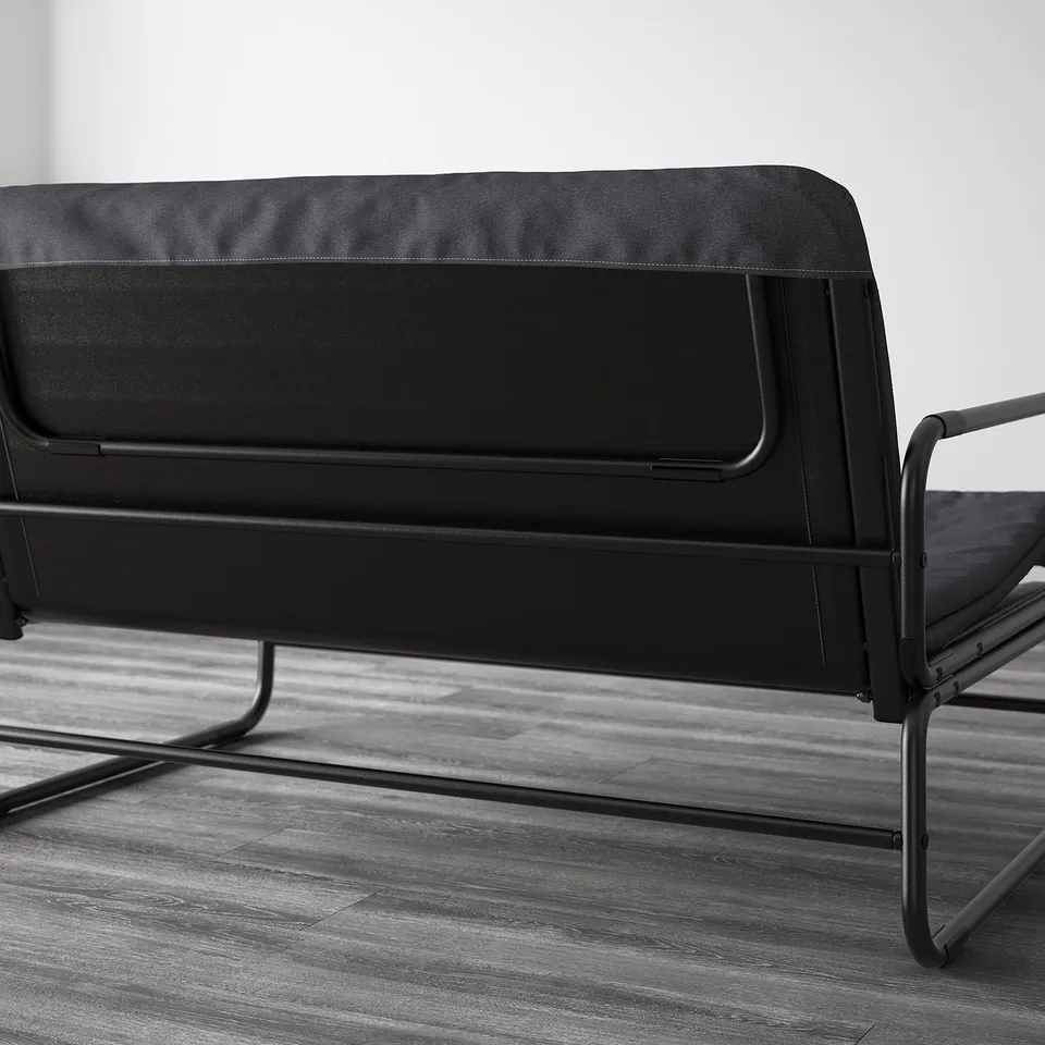 Black sofa bed with metal frame, capable of transforming into a bed for two, shown in a modern room setting.