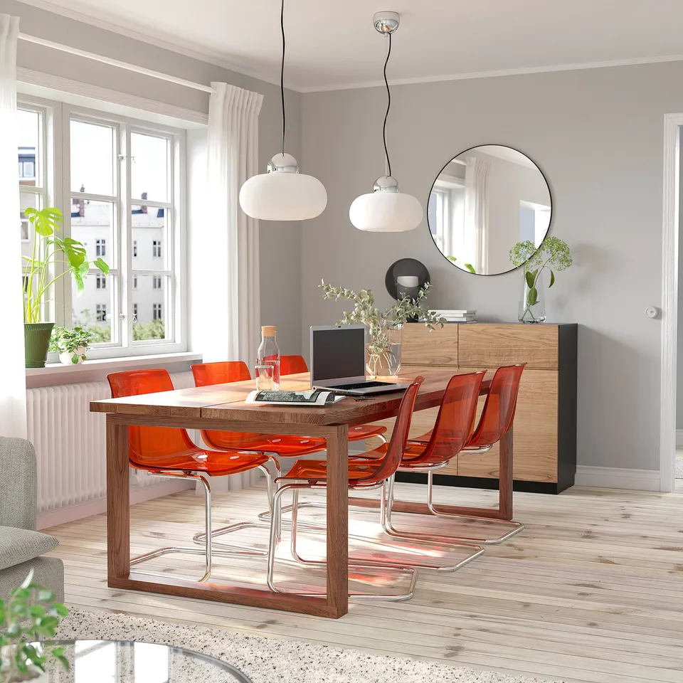 Modern dining setup with MÖRBYLÅNGA table, natural wood, orange chairs, minimalist lights, sideboard, mirror, large window.