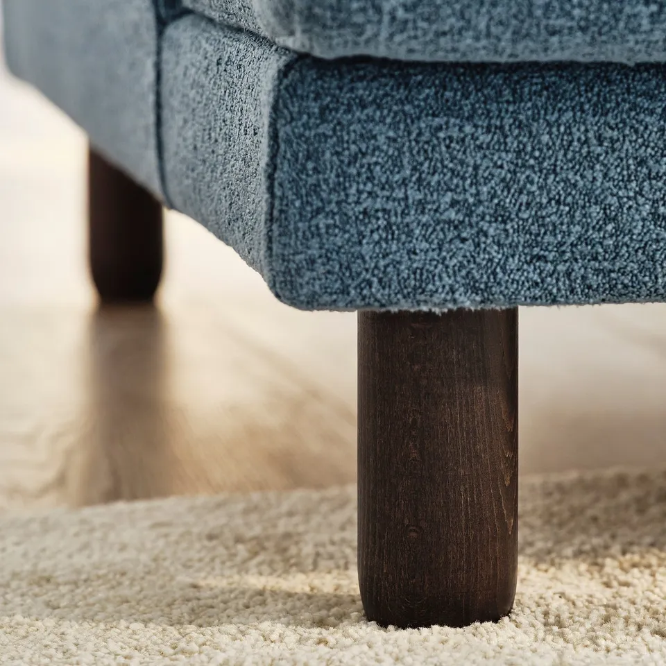 Close-up of a modern sofas robust wooden leg, showcasing quality craftsmanship. Light blue textured fabric meets sturdy support.