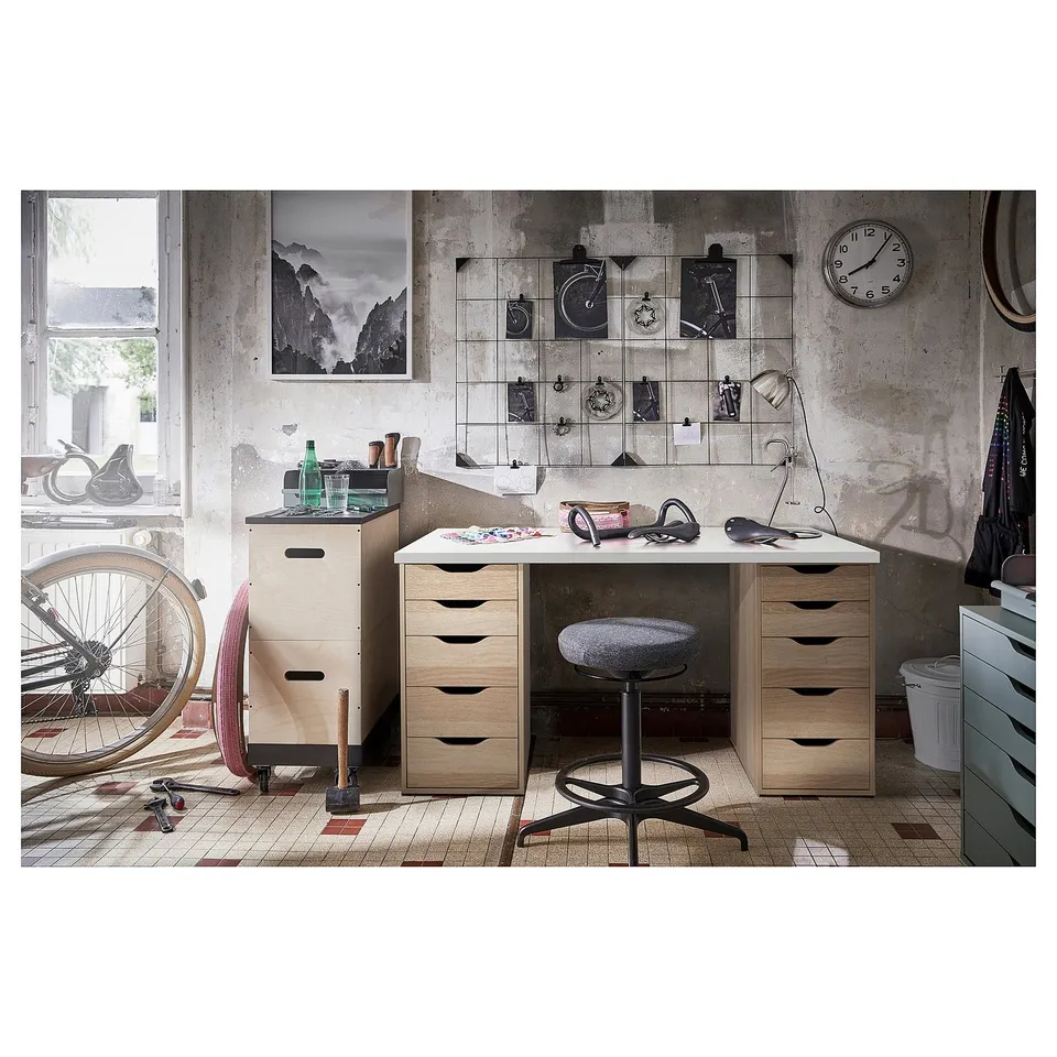 Industrial-style workspace with light wood desk, grey stool, bike, and wall decor.