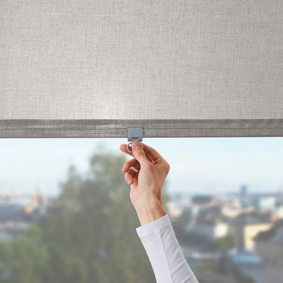 A hand adjusts a LÅNGDANS roller blind, controlling light and privacy. The blinds cordless safety feature, fitting tall windows.