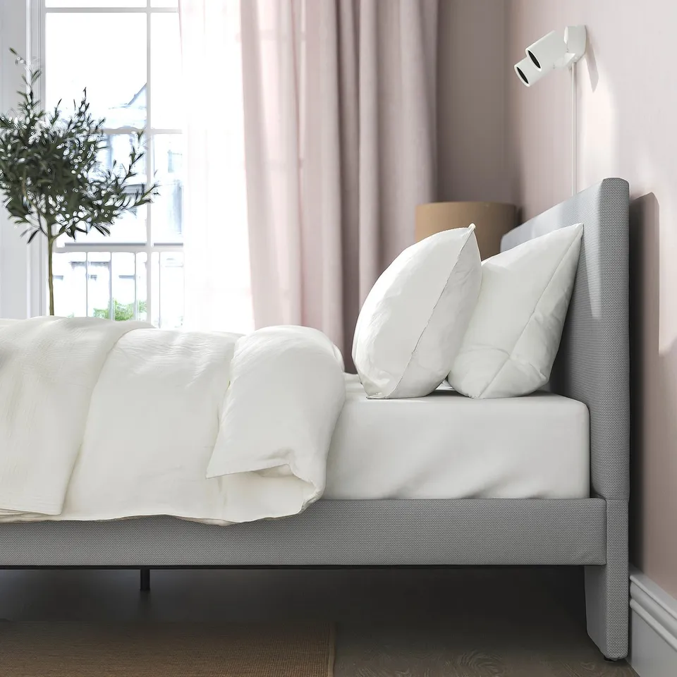 Bed with padded headboard, white linens, by window, horizontal light.