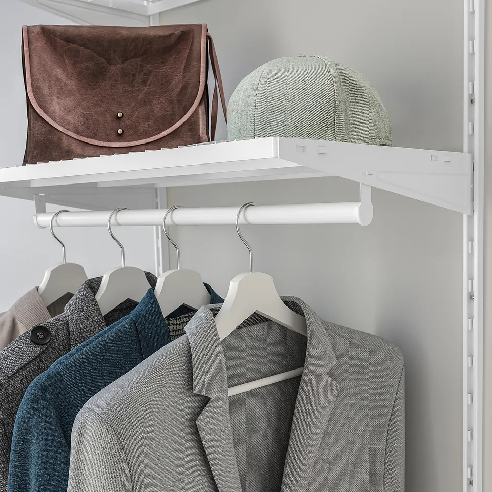 A closet shelf holding a brown bag and green hat above hanging jackets.