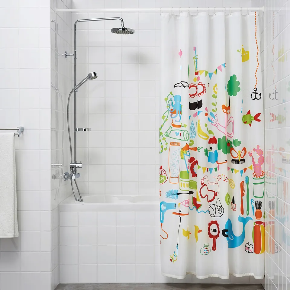A bathroom with a white tiled wall, a shower with a extendable curtain rod and a vibrant shower curtain featuring various cartoonish items.