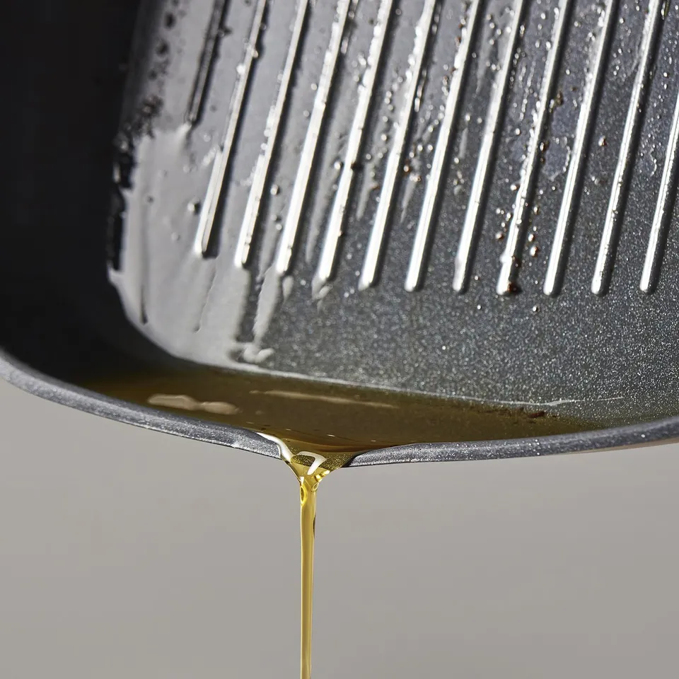Close-up of non-stick grill pan with olive oil being poured, showcasing its non-stick coating.