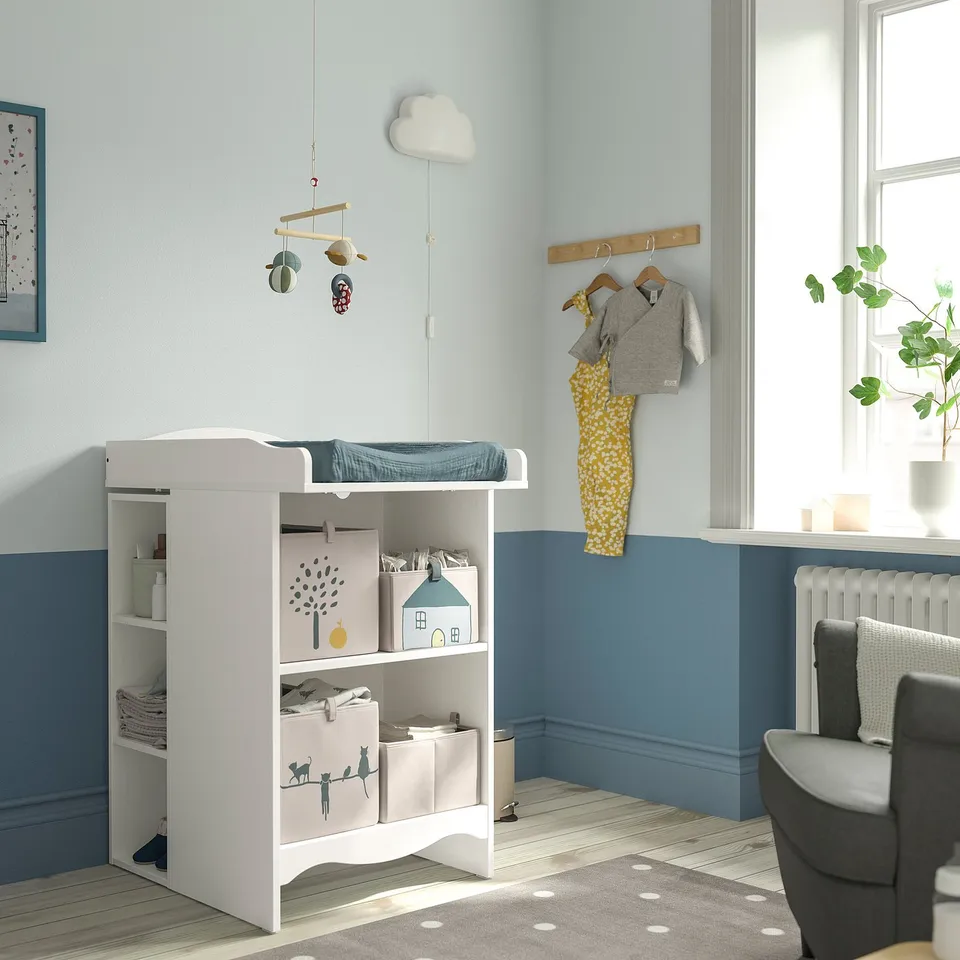 Baby nursery with SMÅGÖRA changing table, blue walls, plant, and grey chair.
