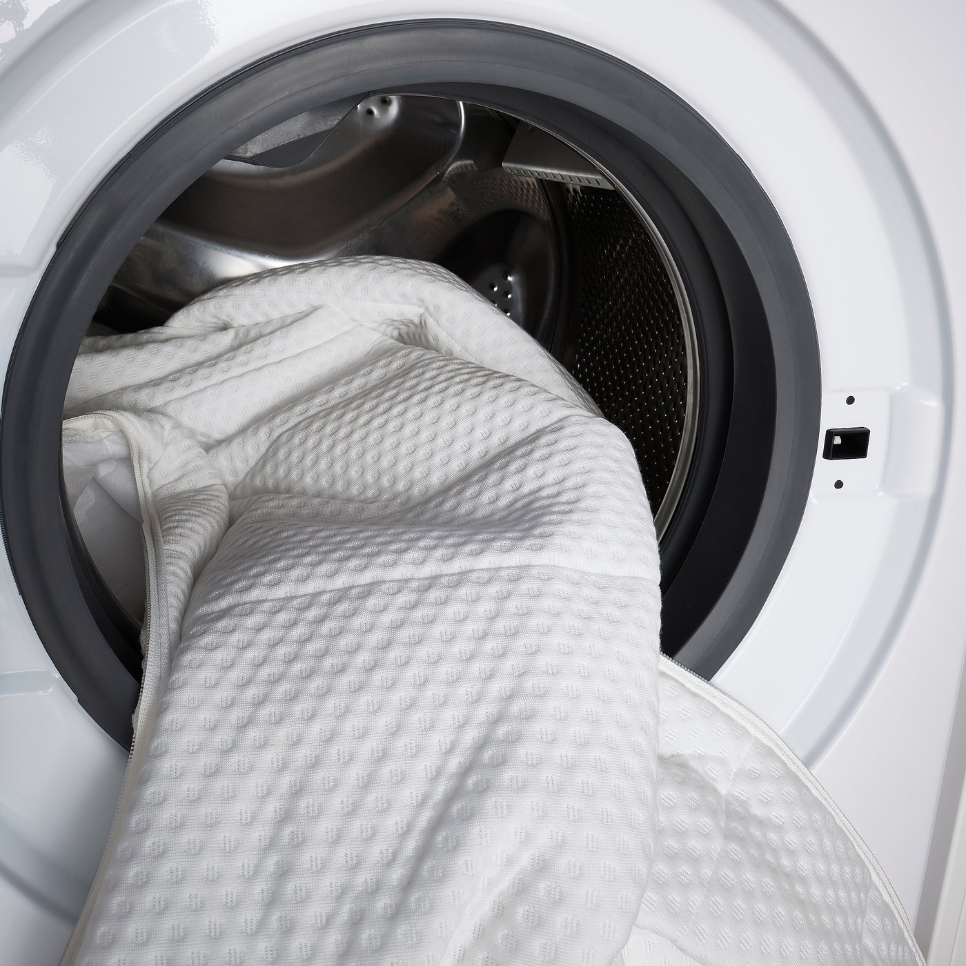 White washing machine with large, textured white blanket inside, ready to clean.