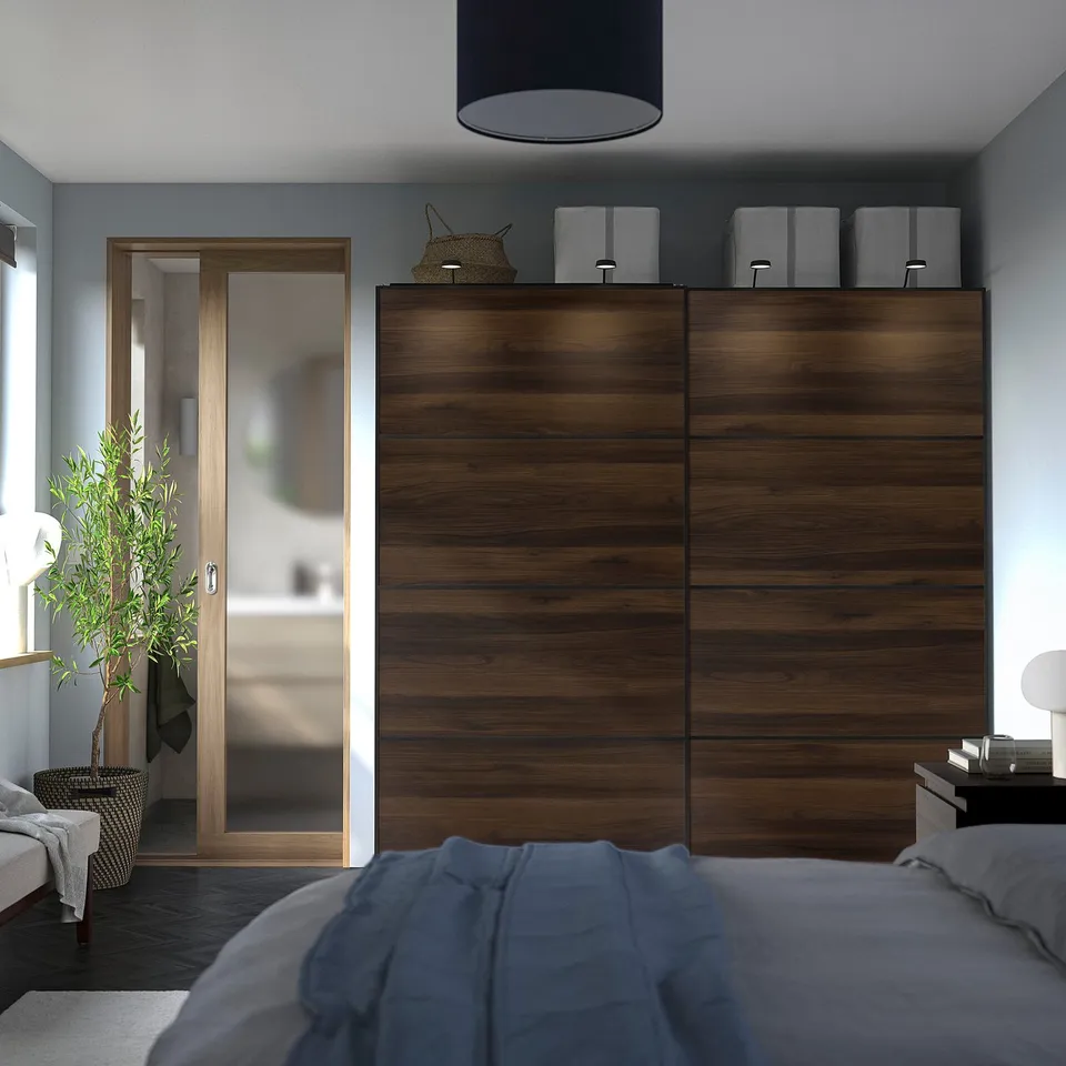 Modern bedroom with large dark MEHAMN wood closet, grey bedding, and small plant. Sliding door saves space.
