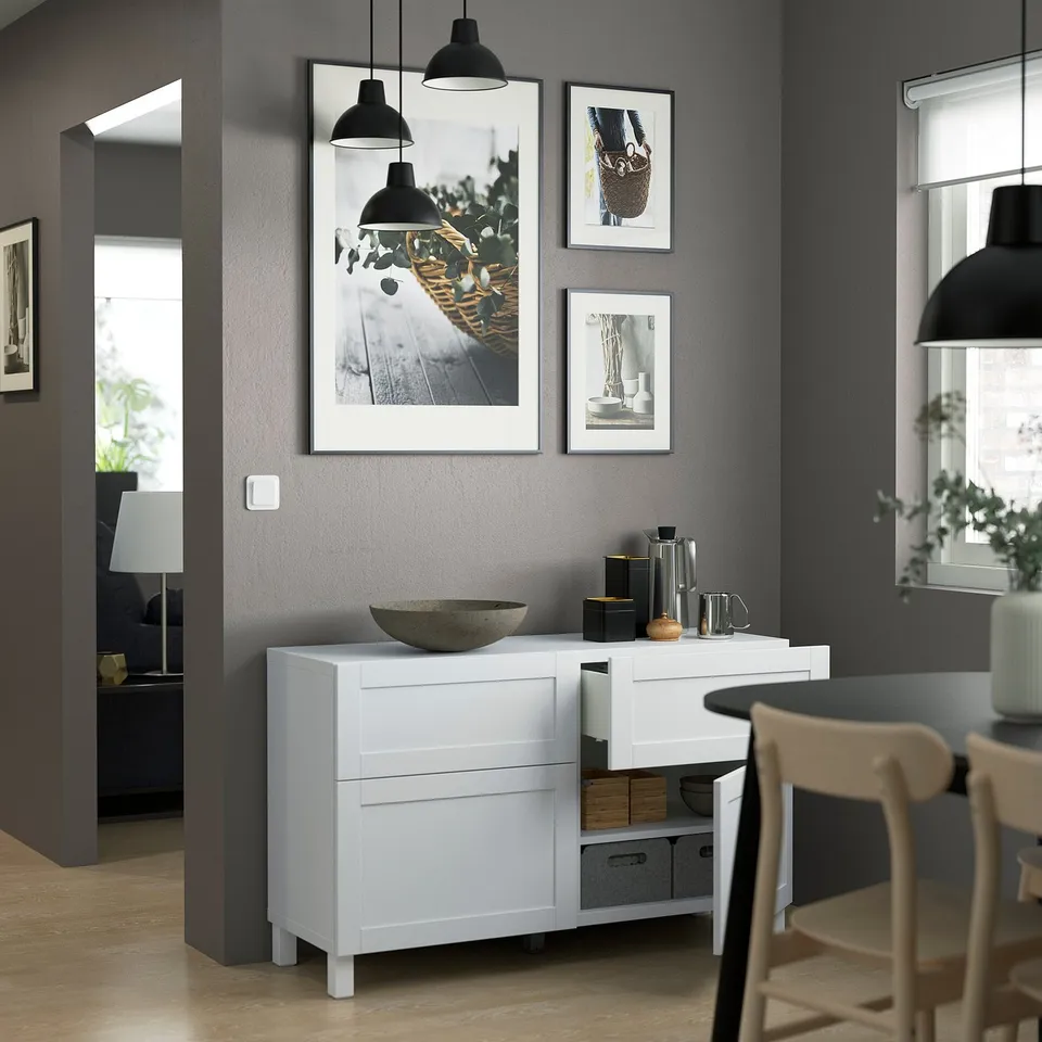 Modern dining room with white cabinet, hanging lights, prints, wooden chairs and potted plants.