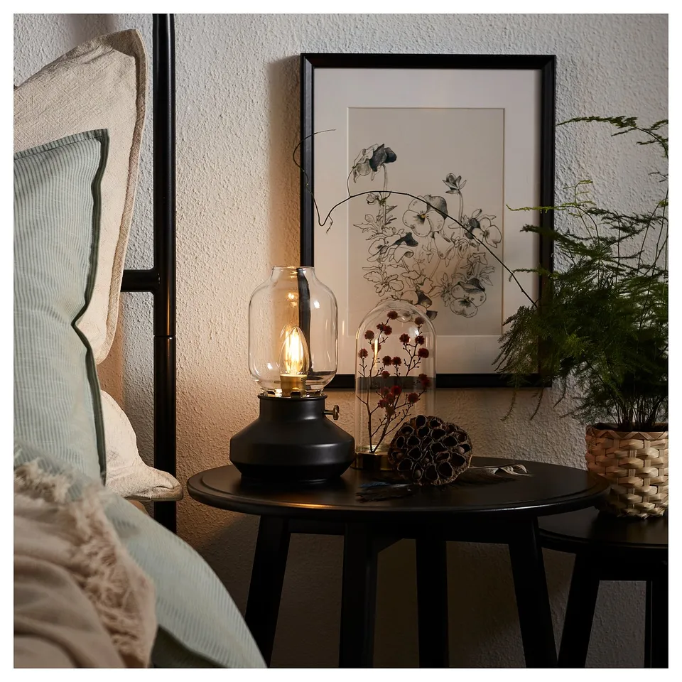 TÄRNABY lamp on table with bulb, floral print, plant in glass, and woven basket.