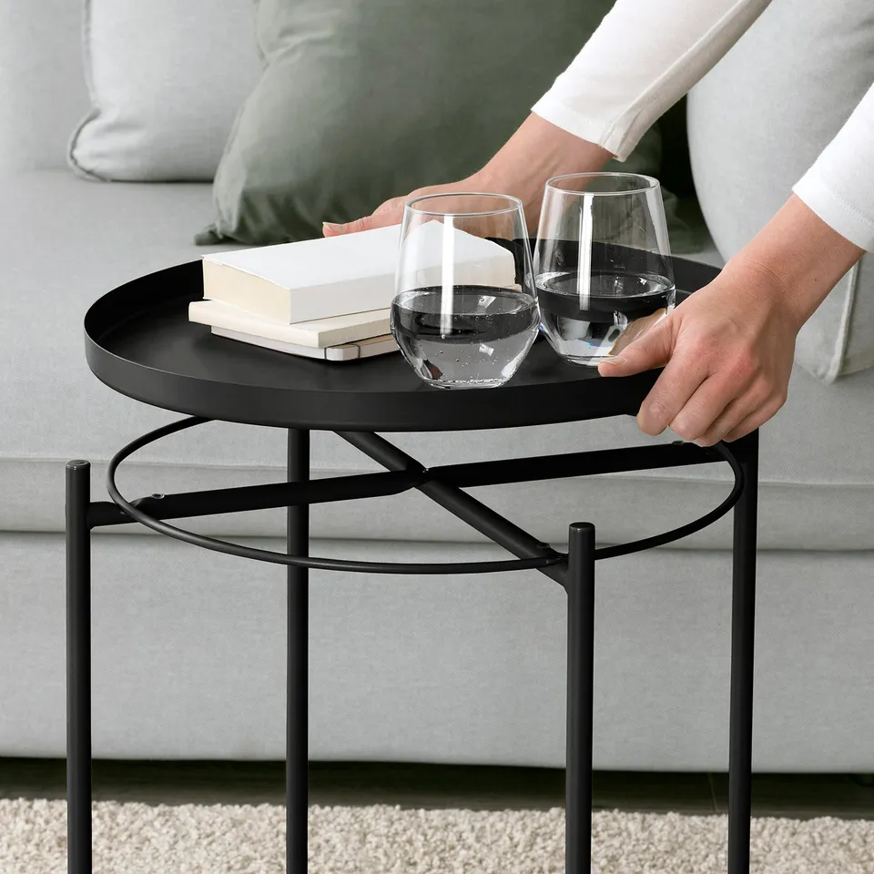 Person hands holding wine glasses on a GLADOM round metal coffee table with tray and books.
