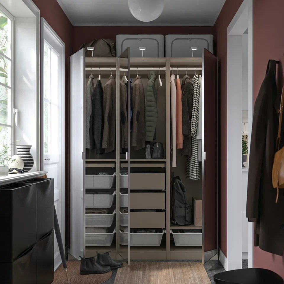 Organised closet with PAX wardrobe, glass doors, silver handles, hanging clothes, shelves, and mesh drawers against red wall.