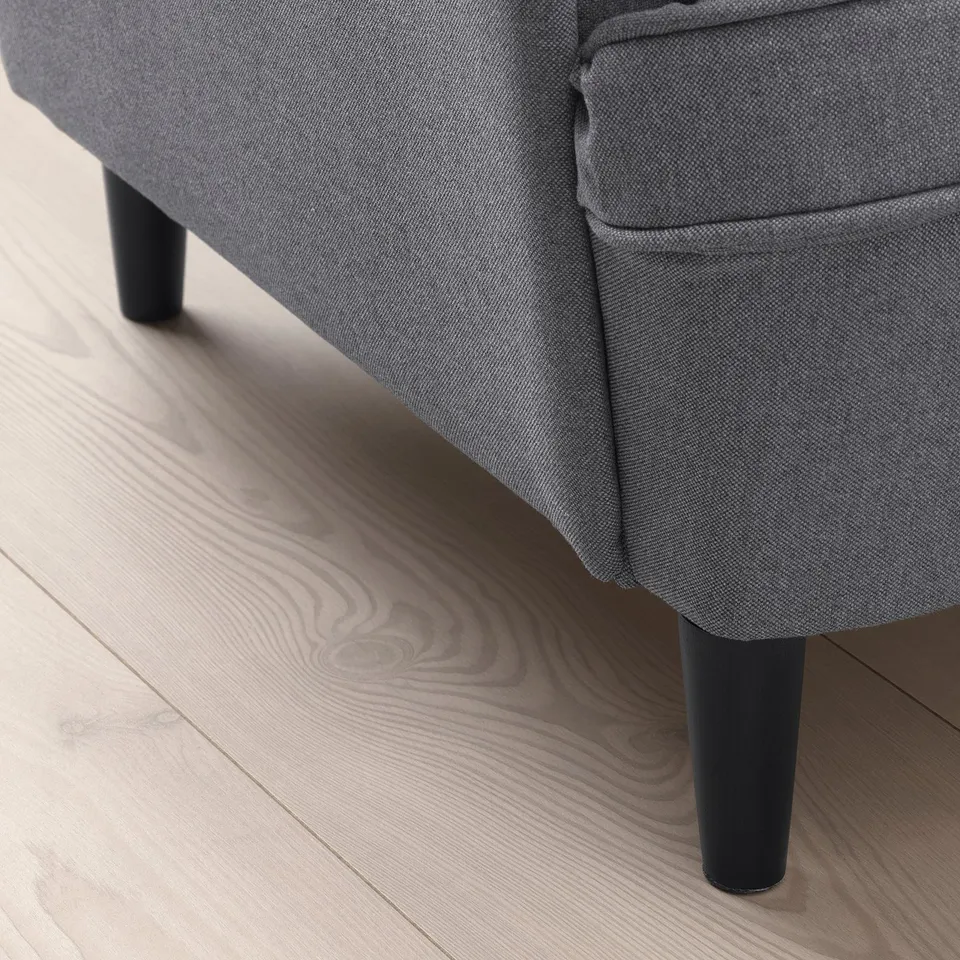 A modern, comfortable grey armchair with black tapered legs on a light wooden floor. The fabric appears durable and the legs are sturdy.